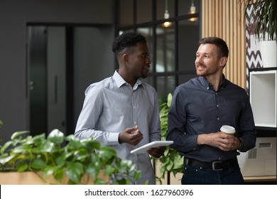 Multiracial Millennial Male Colleagues Stand Having Coffee Break Discussing Startup Project Sharing Business Ideas In Office, Multiethnic Man Coworkers Businessmen Talk Brainstorm At Workplace