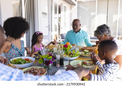 Multiracial multigeneration family holding hands and saying grace at dining table before lunch. Food, drink, unaltered, togetherness, love, childhood, retirement, praying, religion, meal and home. - Powered by Shutterstock