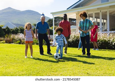 Multiracial Multigeneration Family Looking At Boy Playing Soccer On Grassy Field In Yard In Summer. Unaltered, Togetherness, Childhood, Lifestyle, Retirement, Enjoying And Sport Concept.