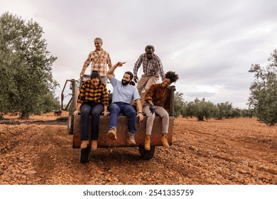 Multiracial and multigenerational farmers are enjoying a moment of celebration, sitting and standing on the trailer of a tractor in an olive orchard, having just finished the harvest - Powered by Shutterstock