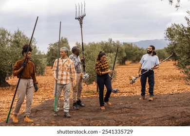 Multiracial and multigenerational group of farmers working together, holding harvesting tools and smiling during olive harvest in an olive orchard - Powered by Shutterstock