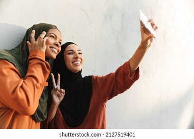 Multiracial muslim women gesturing while taking selfie photo on cellphone outdoors - Powered by Shutterstock