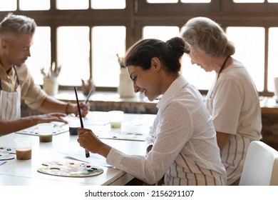 Multiracial painters engaged in painting art class in workshop. Indian artist holds paintbrush drawing on paper sit at table, looks interested, inspired. Art therapy, creative hobby, creation concept - Powered by Shutterstock
