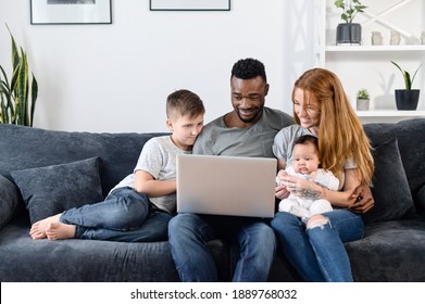 A Multiracial Parents And Their Two Childs On The Sofa With Laptop At Home, Watching Movies, Web Browsing, Playing Game. A Multi Ethnic Family Spend Time With With Gadget