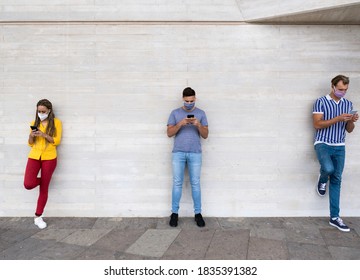 Multiracial People Standing In A Line With Social Distance And Looking At Smartphones While Wearing Protective Face Mask - Coronavirus Lifestyle