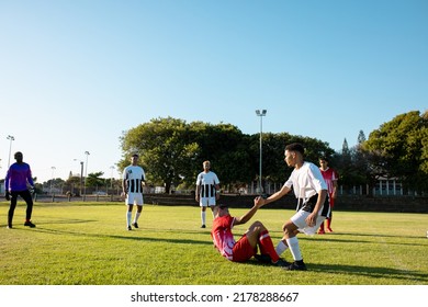 Multiracial player holding hand and assisting injured opponent to get up during match at playground. Copy space, pain, summer, unaltered, rivalry, soccer, team sport, competition and sport concept.