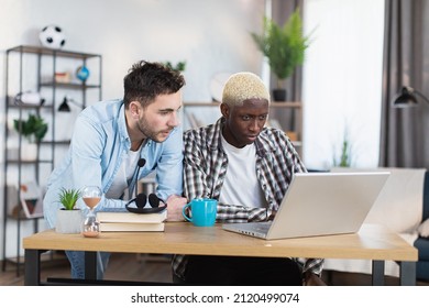 Multiracial Same Sex Couple Of Two Handsome Gays Using Modern Laptop Ai Living Room. African American Man Sitting At Desk While Caucasian Standing Near.