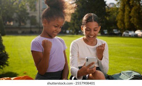 Multiracial school students pupils schoolgirls girls using mobile phone outdoors children African American little kids friends classmates gadget addict smartphone play online game happy win celebrate - Powered by Shutterstock