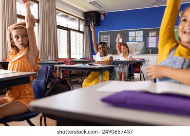 Multiracial schoolgirls raising their hands while sitting at desks in classroom. Unaltered, education, student, german, school, childhood, learning, question, answering concept. - Powered by Shutterstock