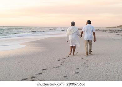 Multiracial senior couple holding hands walking together while leaving footprints on sand. lifestyle, love and weekend. - Powered by Shutterstock