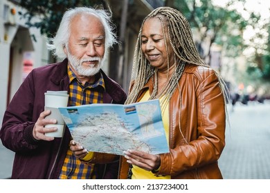 Multiracial senior couple looking for directions on map outdoor - Elderly travelers and healthy lifestyle - Focus on African woman face - Powered by Shutterstock