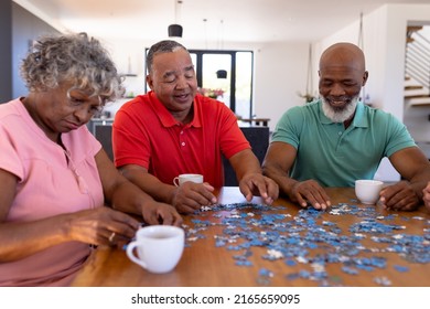 Multiracial senior friends arranging jigsaw pieces on table while enjoying coffee in nursing home. Puzzle, game, confusion, brainstorming, unaltered, togethern, support, assisted living, retirement. - Powered by Shutterstock