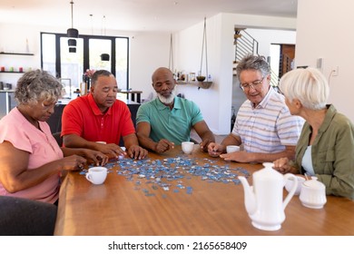 Multiracial senior friends with coffee cups on table solving jigsaw puzzle in nursing home. Game, pieces, confusion, brainstorming, unaltered, togetherness, support, assisted living, retirement. - Powered by Shutterstock