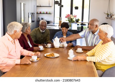 Multiracial senior friends having coffee and cookies while sitting at dining table in nursing home. Snacks, drink, food, unaltered, friendship, togetherness, support, assisted living and retirement. - Powered by Shutterstock