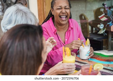 Multiracial senior friends having fun outdoor at bar restaurant while drinking no alcohol cocktails - Focus on african woman face - Powered by Shutterstock