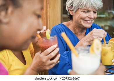 Multiracial senior friends having fun while drinking no alcohol cocktails outdoor at bar restaurant - Focus on right woman face - Powered by Shutterstock