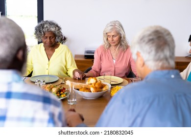 Multiracial Senior Friends Holding Hands And Saying Grace At Dining Table In Nursing Home. Food, Praying, Togetherness, Lunch, Unaltered, Support, Assisted Living And Retirement Concept.