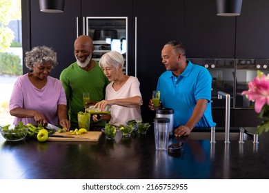 Multiracial senior men holding glasses with smoothie and looking at females preparing it in kitchen. Retirement home, unaltered, togetherness, support, assisted living and healthy food concept. - Powered by Shutterstock