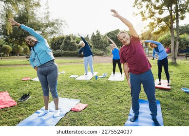 Multiracial senior people doing stretching workout exercises outdoor with city park in background - Healthy lifestyle and joyful elderly lifestyle concept - Focus on right man face - Powered by Shutterstock