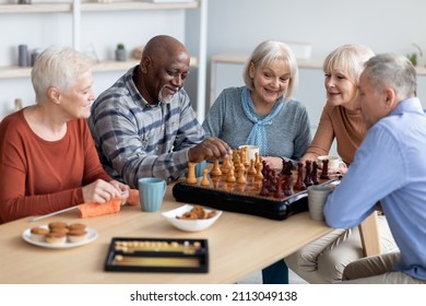 Multiracial senior people men and women in casual playing chess at nursing home, sitting around table, drinking tea with cookies, playing table games, knitting, spending time together - Powered by Shutterstock