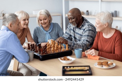 Multiracial senior people men and women in casual playing chess at nursing home, sitting around table, drinking tea with cookies, playing table games, knitting, spending time together - Powered by Shutterstock