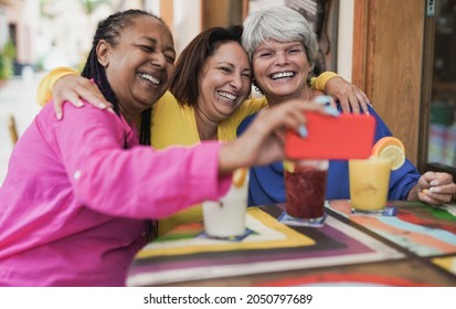 Multiracial Senior Women Taking A Selife Using Mobile Phone At Bar Outdoor - Elderly Girlfriends Enjoy Healthy Smoothie And Having Fun With Technology