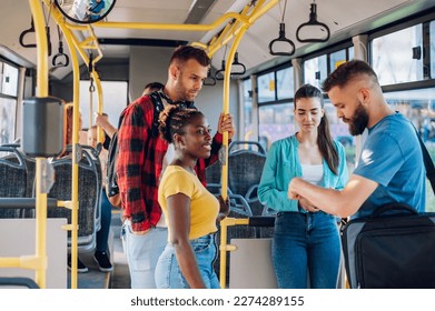 Multiracial smiling group of friends standing in a bus and talking while riding together. Diverse passengers enjoying city ride. Young people students using public transport in a big city. - Powered by Shutterstock