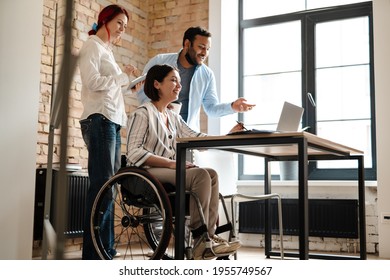 Multiracial smiling three colleagues talking and working with laptop in office - Powered by Shutterstock