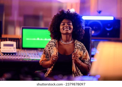 A multiracial sound technician sitting in a chair in front of mixing console in music studio. Portrait of a cheerful young music producer sitting in a recording studio while smiling at the camera. - Powered by Shutterstock