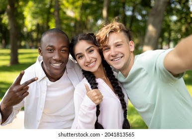 Multiracial students friends making selfie, gesturing v-sign and showing thumb up, posing outdoors in campus. Teens happy about entering university