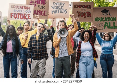 Multiracial Students Protesting for Education - Diverse group of young students marching, raising clenched fists and holding signs advocating for change in education. - Powered by Shutterstock