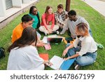 Multiracial students using a laptop computert sitting in a circle on the grass, doing homework outside at university campus. Young high school people working together on a academy task or schoolwork