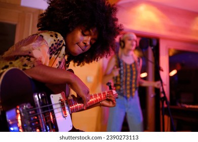 A multiracial talented bass player while playing bass, improvising and recording with a female vocalist. Portrait of a bass player sitting in a musical studio and recording a song with a singer. - Powered by Shutterstock