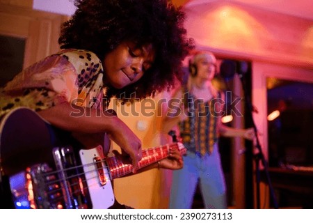 A multiracial talented bass player while playing bass, improvising and recording with a female vocalist. Portrait of a bass player sitting in a musical studio and recording a song with a singer.
