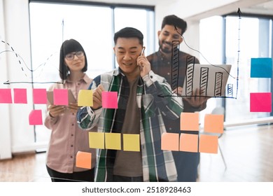 Multiracial team collaborating during business meeting with colorful sticky notes and bar charts. Coworkers brainstorming strategy ideas on transparent board, each person in project planning. - Powered by Shutterstock