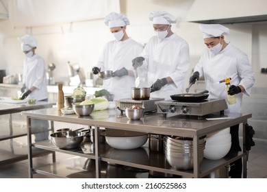 Multiracial team of cooks in uniform and face masks cooking meals for a restaurant in the kitchen. Concept of teamwork at restaurant during pandemic. Latin, Asian and European guys cooking together - Powered by Shutterstock