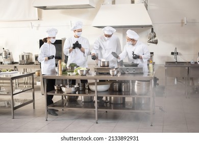 Multiracial team of cooks in white uniform cooking together in restaurant kitchen. Concept of teamwork and hard work at restaurant. Cooks wearing face masks to prevent virus spread  - Powered by Shutterstock