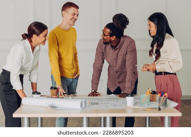 Multiracial team of engineers or architects being happy for solving a problem of a a project they are working on. All together smiling while talking and standing gathered around the table. Copy space. - Powered by Shutterstock