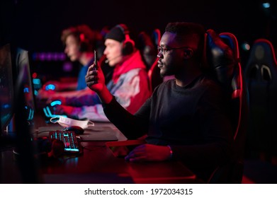 A multi-racial team of esports athletes conducts a training session before an online shooter tournament. Neon light.