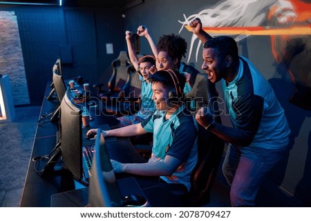 Multiracial team of happy professional cyber sports gamers celebrating success wile raising hands up during esports tournament in gaming club