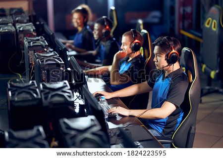 Multiracial team of professional cybersport gamers wearing headphones participating in global eSport tournament, playing online video games, side view