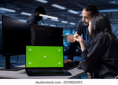 Multiracial team reconfiguring server farm to optimize it for data processing using green screen laptop. Diverse coworkers ensuring data center equipment operates efficiently using mockup notebook