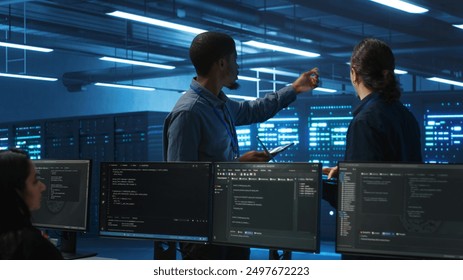 Multiracial team of technicians working in high tech server hub capable of storing vast amounts of data. Coworkers doing brainstorming, trying to troubleshoot servers controlling network resources