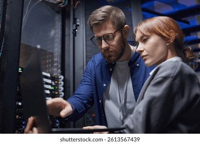 Multiracial team working on server maintenance in a data center. Man and woman collaborating while examining server rack and discussing technical details