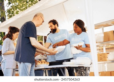 Multiracial team working together at food drive, charitably distributing essential items to less fortunate. Multiethnic people wearing blue t-shirts providing hunger relief and volunteer assistance.