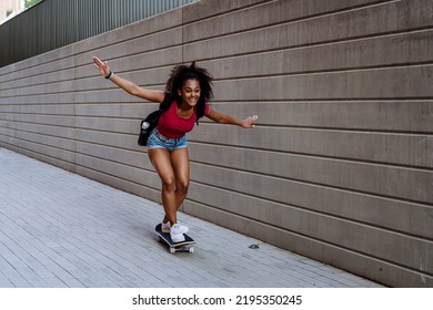 Multiracial teenage girl riding a skateboard in front of concrete wall, balancing. Side view. - Powered by Shutterstock