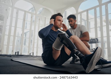 Multiracial trainer next to young man in sportswear with prosthetic leg doing push-ups at the gym - Powered by Shutterstock