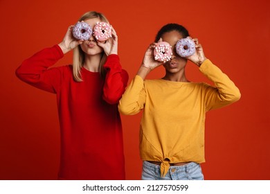 Multiracial two girls grimacing while making fun with donuts isolated over red wall - Shutterstock ID 2127570599