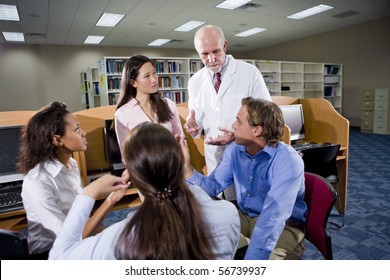 Multiracial University Students With Professor Conversing In Library