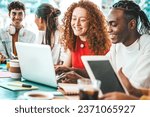 Multiracial university students sitting together at table with books and laptop - Happy young people doing group study in high school library - Life style concept with guys and girls in college campus